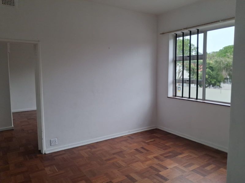 An empty bedroom featuring classic parquet flooring, white walls, and a window fitted with security bars, offering a blank canvas for personalization.