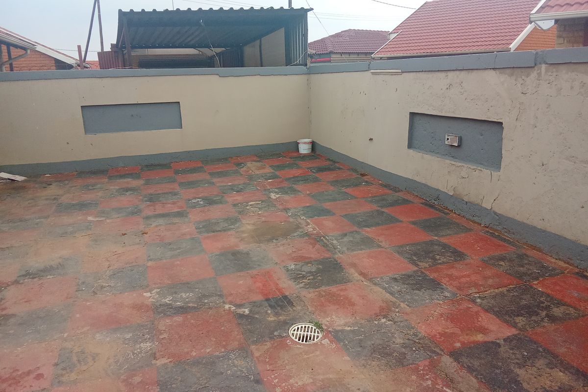 An outdoor patio area featuring a checkerboard tiled floor and perimeter boundary walls, requiring maintenance and cosmetic updates to improve its overall appearance.