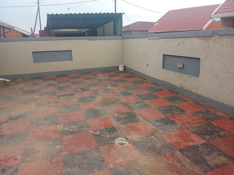 An outdoor patio area featuring a checkerboard tiled floor and perimeter boundary walls, requiring maintenance and cosmetic updates to improve its overall appearance.