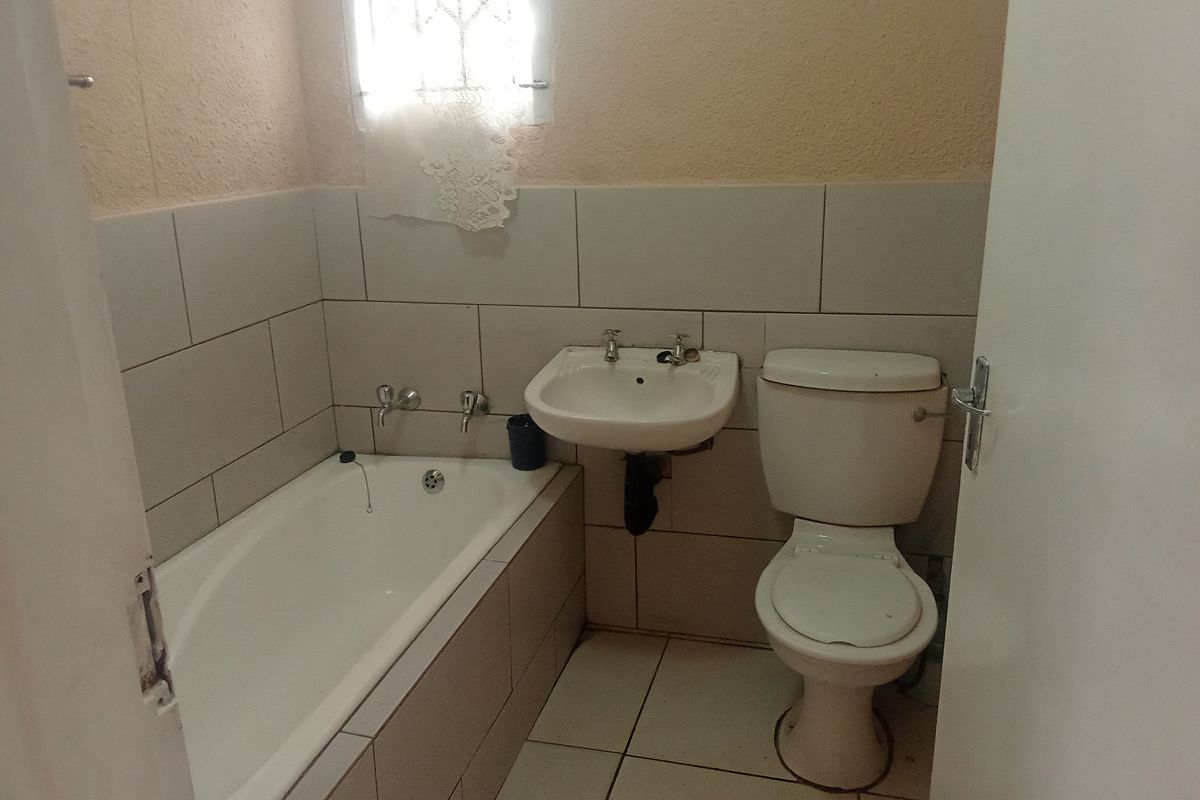 A functional bathroom featuring a bathtub, wall-mounted basin, and toilet with neutral wall and floor tiling.
