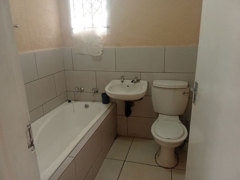 A functional bathroom featuring a bathtub, wall-mounted basin, and toilet with neutral wall and floor tiling.