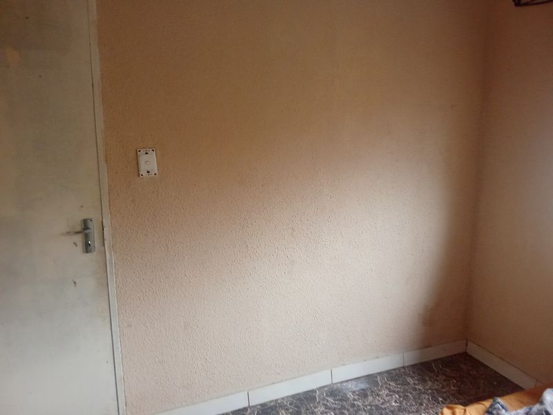 A small, empty bedroom featuring textured walls, a standard internal door, and tiled skirting boards, requiring cosmetic updates.