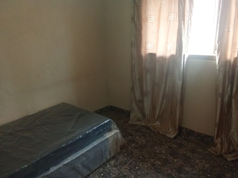 A simple bedroom featuring tiled flooring and a window with curtains, presenting a blank canvas for potential interior updates.