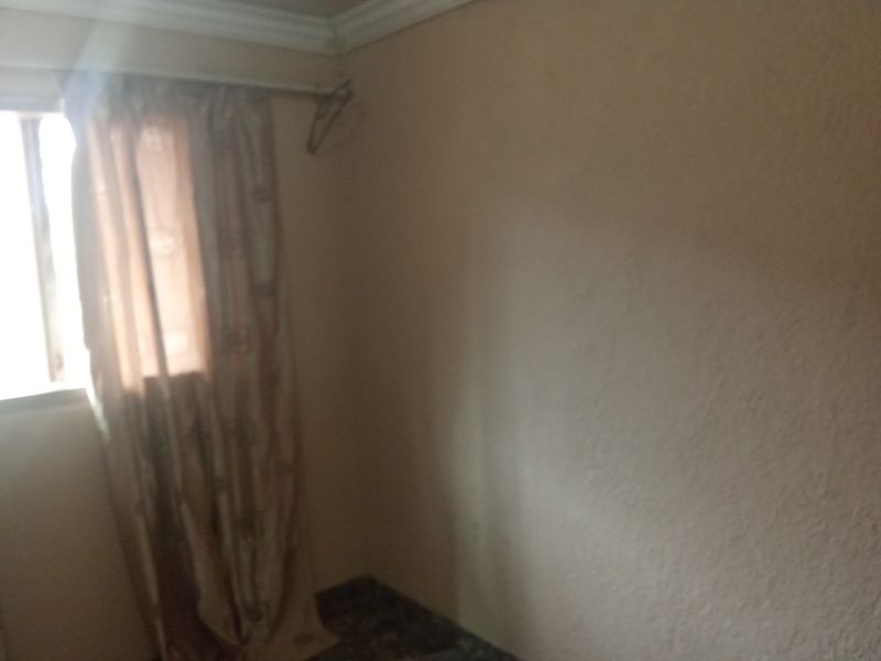 A simple, empty bedroom featuring plain walls, a window with a curtain rail, and decorative ceiling cornice.