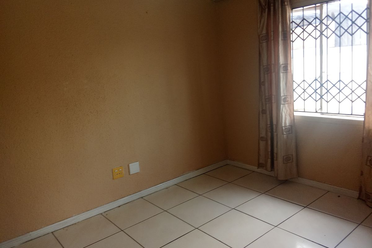 An empty bedroom featuring tiled flooring, a window with a security gate, and neutral wall finishes.