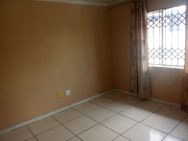 An empty bedroom featuring tiled flooring, a window with a security gate, and neutral wall finishes.