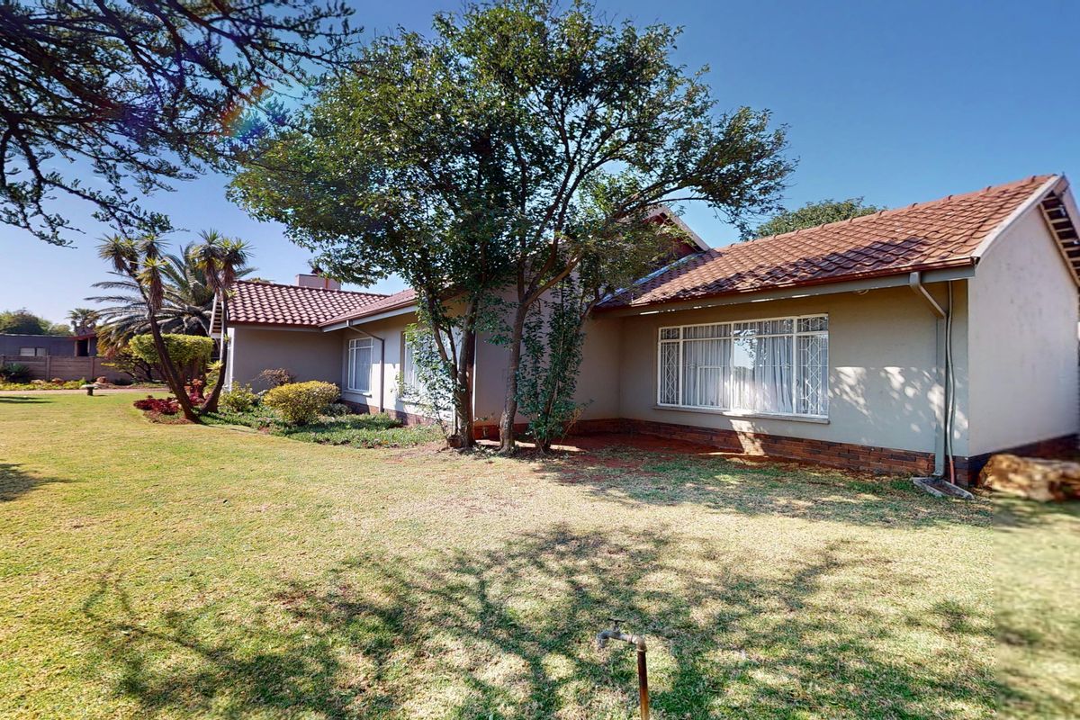 Rear view of the house featuring a tiled roof, brick plinth, and a spacious garden area with established trees.