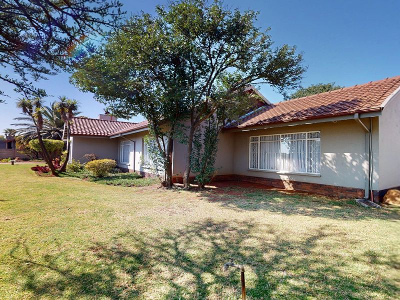 Rear view of the house featuring a tiled roof, brick plinth, and a spacious garden area with established trees.