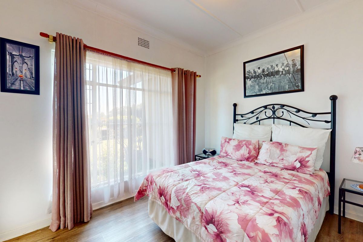 A well-lit bedroom featuring laminate flooring, neutral walls, and a large window with curtain fixtures.