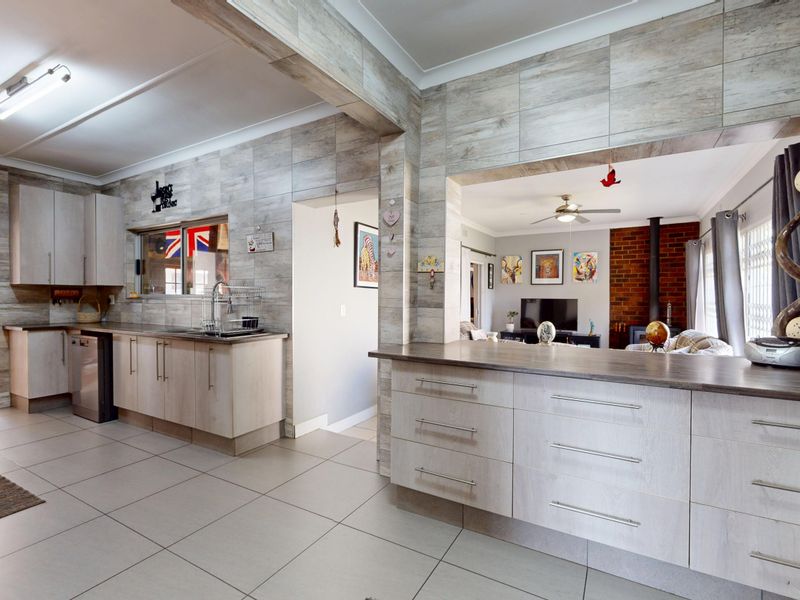 Open plan kitchen and living area featuring modern wood-look cabinetry, tiled flooring, a breakfast bar, and a cozy brick fireplace in the adjacent lounge.