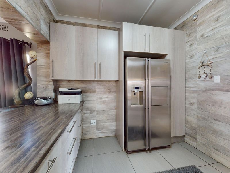 A functional kitchen area featuring light wood-look cabinetry, dark laminate countertops, and neutral floor tiles.