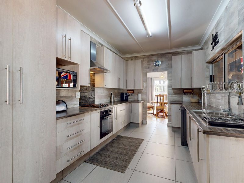 Modern galley-style kitchen featuring light wood-grain cabinetry, integrated appliances, tiled backsplash, and durable tiled flooring with a functional layout.
