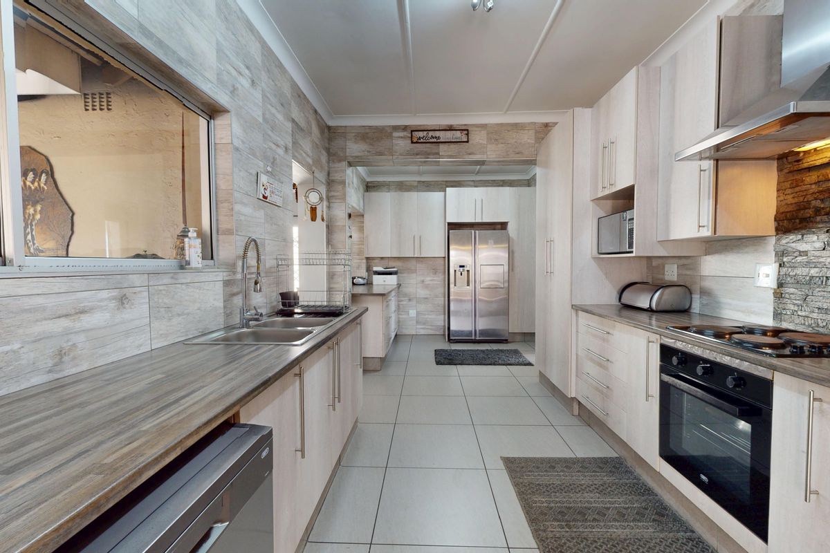 Modern kitchen featuring light wood-look cabinetry, stone feature wall, stainless steel appliances, and durable tiled flooring with ample counter space.