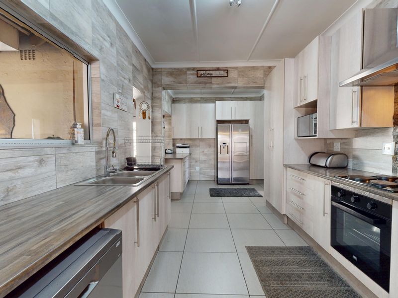 Modern kitchen featuring light wood-look cabinetry, stone feature wall, stainless steel appliances, and durable tiled flooring with ample counter space.