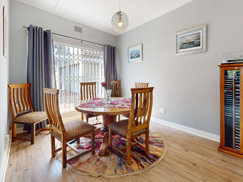 A well-maintained dining room featuring laminate flooring, a central pendant light, and a secure window with a fitted security gate.