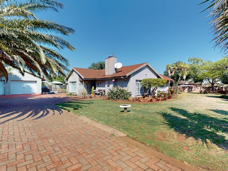 Front view of a single-story house featuring a brick-paved driveway, double garage, and a well-maintained garden with mature palm trees.