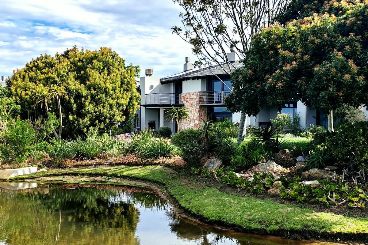 A scenic view of the rear elevation of the apartment building, featuring stone accents, balconies, and a well-maintained garden overlooking a pond.