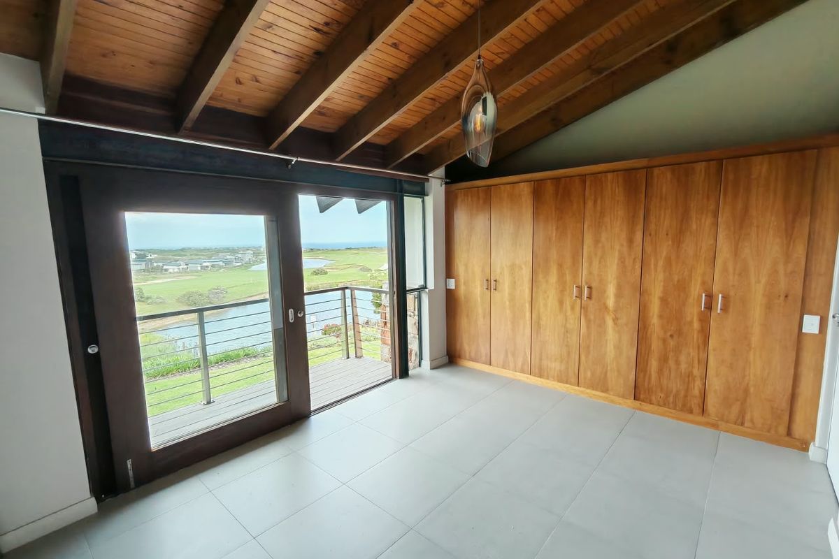 Spacious bedroom featuring exposed timber beam ceilings, built-in wooden cabinetry, tiled flooring, and direct access to a balcony with scenic views.