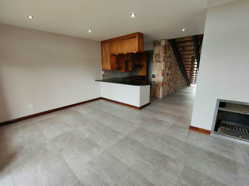 Open-plan living area featuring a modern kitchen with granite countertops, a stone feature wall, built-in fireplace, and neutral porcelain floor tiles.