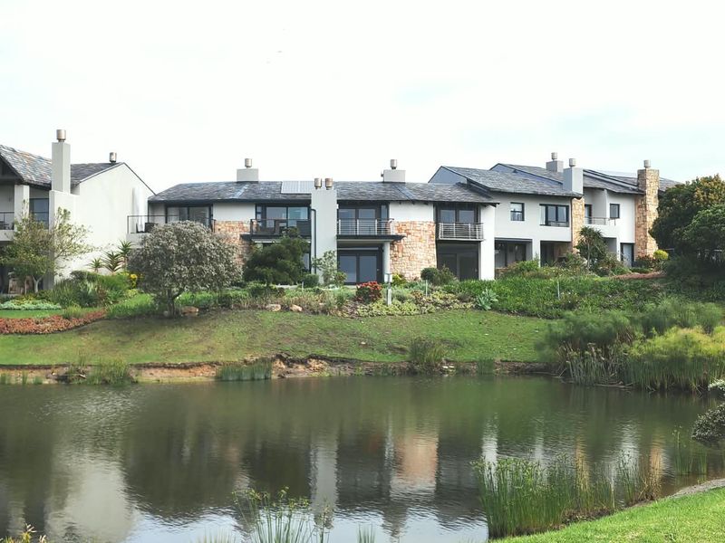 A view of the rear elevation of a modern apartment complex featuring stone accents, balconies, and well-maintained gardens overlooking a pond.