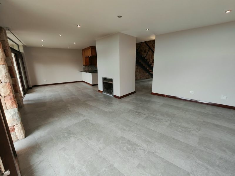 Spacious open-plan living area featuring modern tiled floors, a built-in fireplace, stone accent wall, and an integrated kitchen with granite countertops.