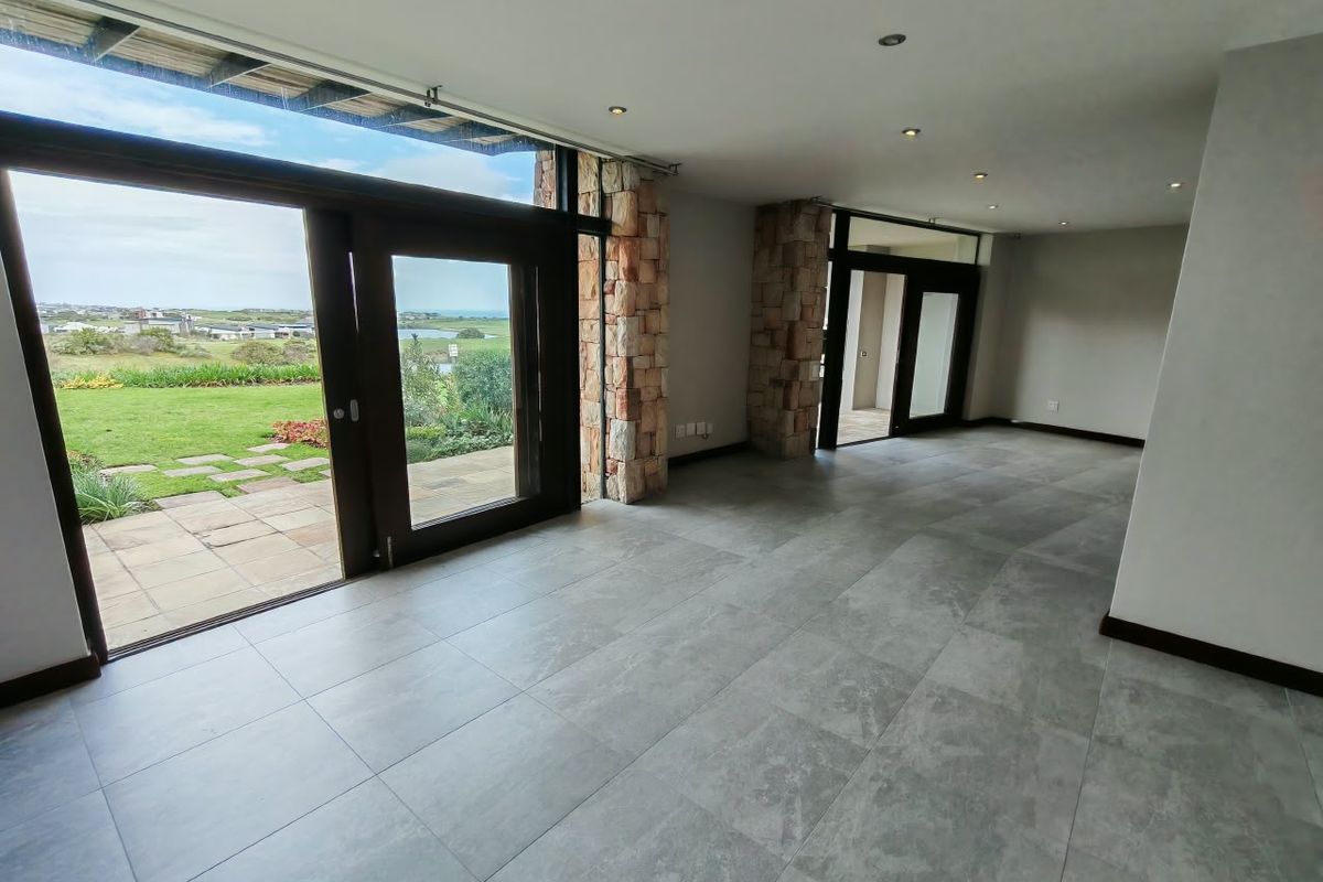 Spacious open-plan living area featuring large format floor tiles, stone-clad pillars, and expansive glass doors opening to a garden view.