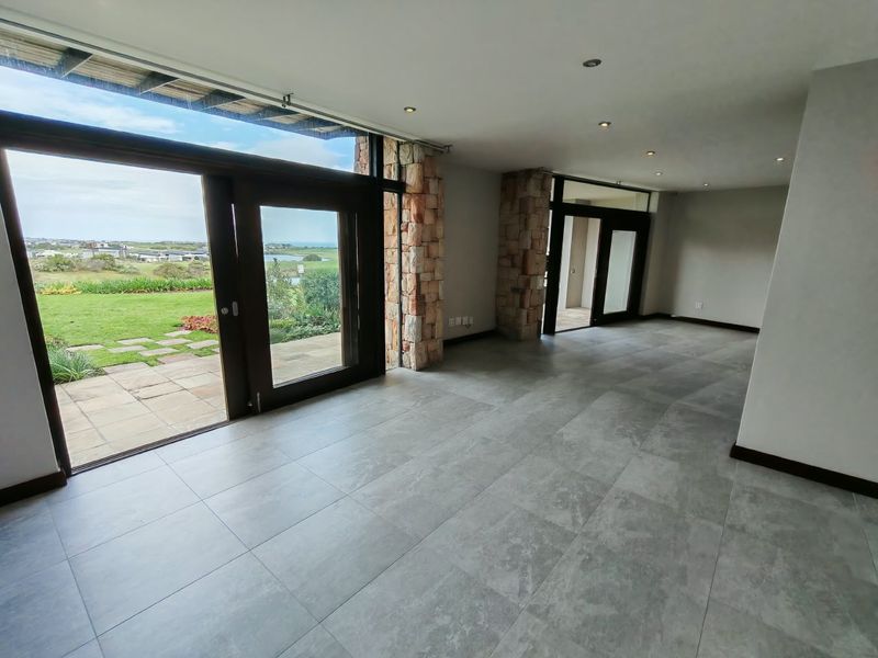 Spacious open-plan living area featuring large format floor tiles, stone-clad pillars, and expansive glass doors opening to a garden view.