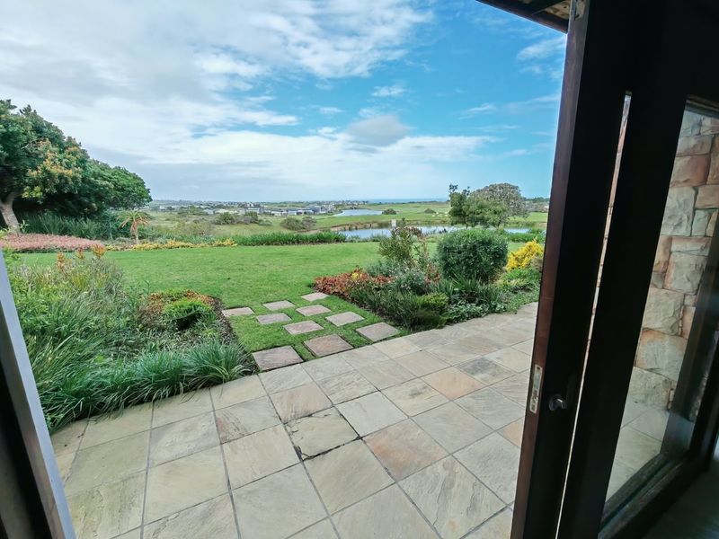 A stone-paved patio area overlooking a landscaped garden and scenic estate view, framed by a timber door structure.