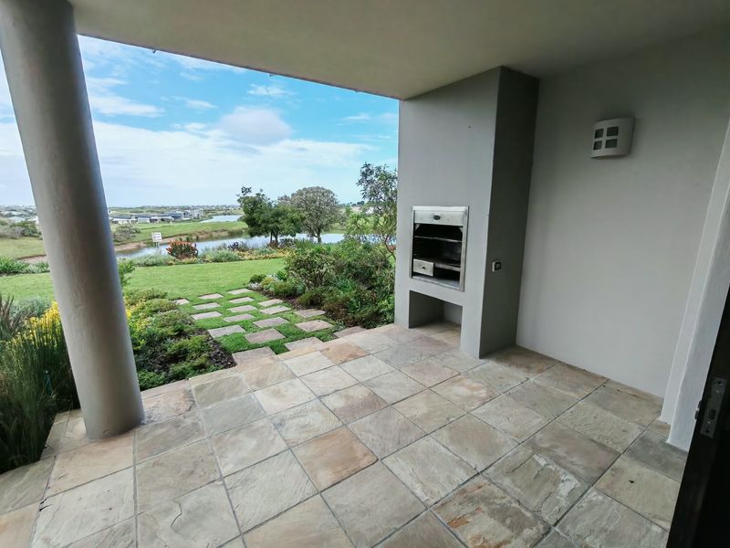 Covered patio featuring stone tile flooring and a built-in braai, overlooking a landscaped garden and scenic water view.