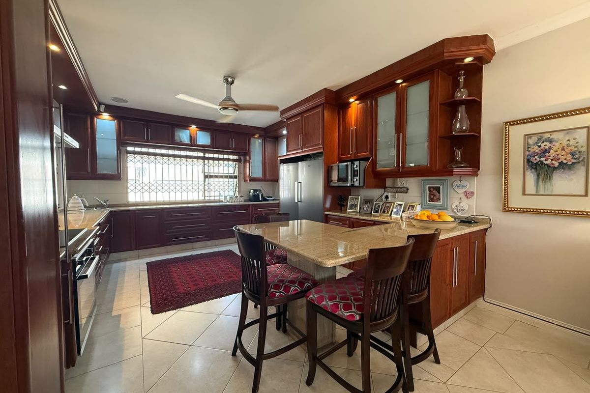 Spacious kitchen featuring dark wood cabinetry, granite countertops, a central island with breakfast bar seating, and tiled flooring.