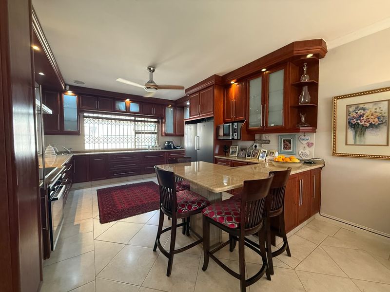 Spacious kitchen featuring dark wood cabinetry, granite countertops, a central island with breakfast bar seating, and tiled flooring.