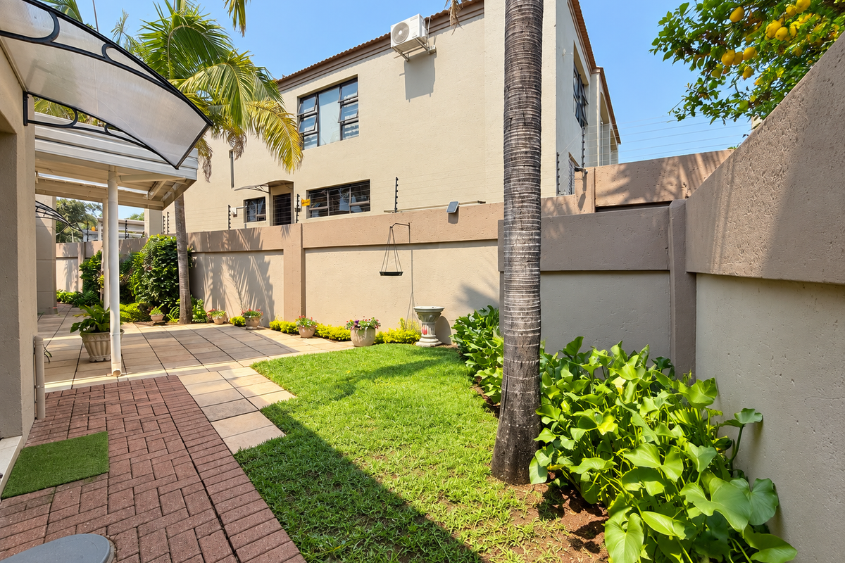 A well-maintained rear garden featuring a paved patio area, lawn, and secure boundary walls with electric fencing.