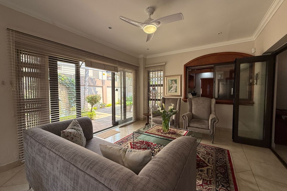 A bright living room featuring tiled flooring, a ceiling fan, and large sliding glass doors that provide direct access to the outdoor patio area.