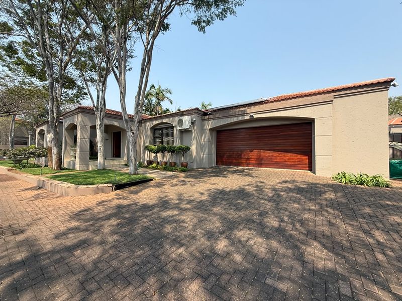 Front elevation of a well-maintained house featuring a paved driveway, double garage with a wooden door, and established garden landscaping.