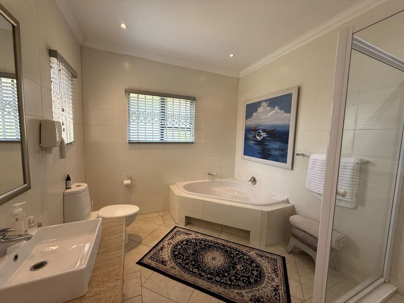 A well-maintained bathroom featuring a corner bathtub, separate shower enclosure, vessel sink on a stone vanity, and neutral wall and floor tiling.