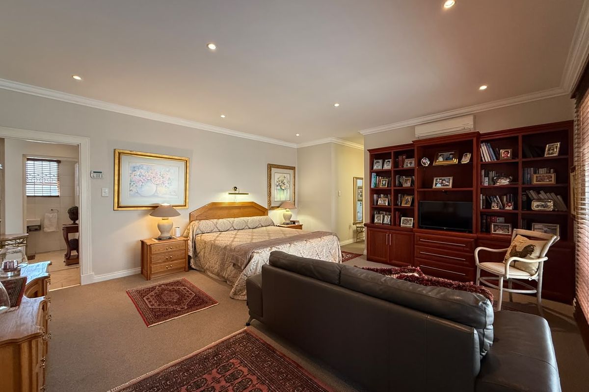 Spacious bedroom featuring built-in cabinetry, recessed downlighting, and an adjoining en-suite bathroom, offering a comfortable and well-maintained living space.