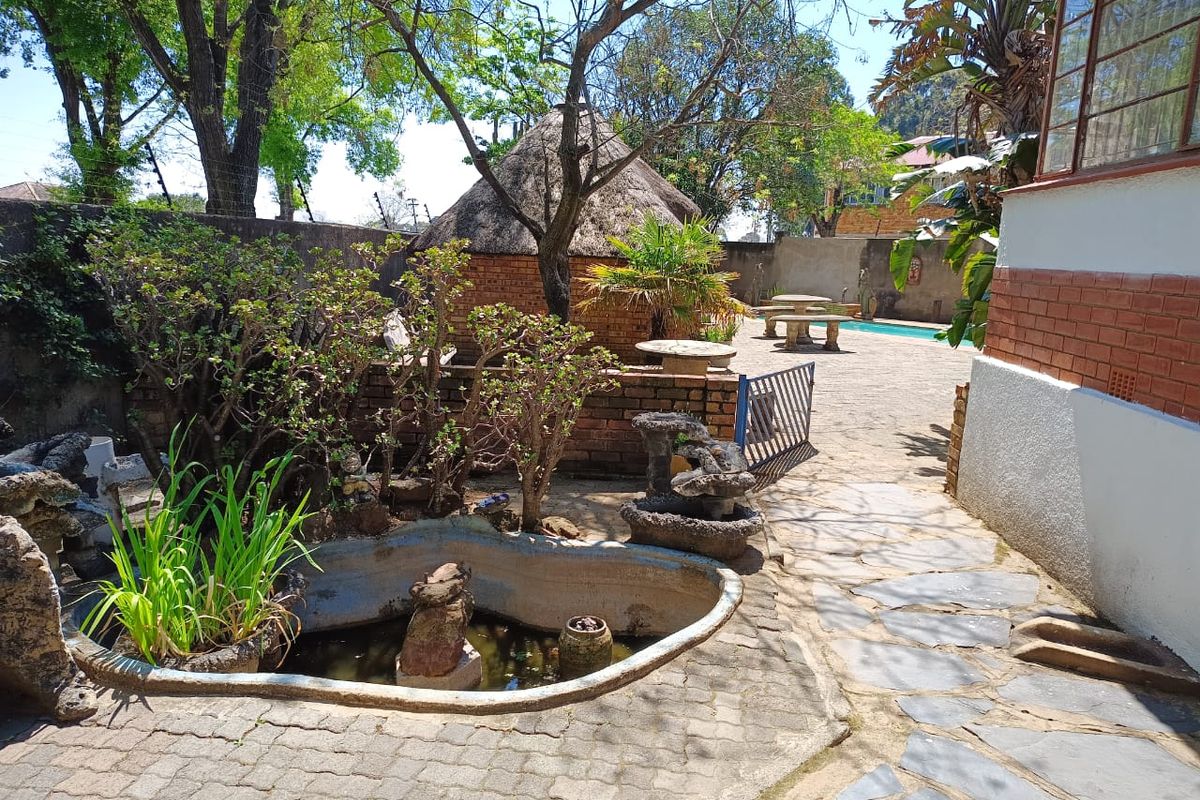 Rear garden area featuring a swimming pool, a traditional thatched lapa, stone paving, and a decorative water feature within a walled perimeter.