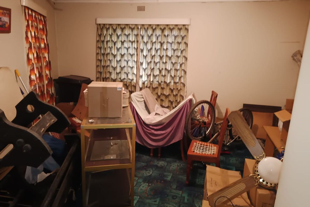 A bedroom space featuring a ceiling fan and patterned carpeting, currently in need of renovation and clearing to restore its functionality.