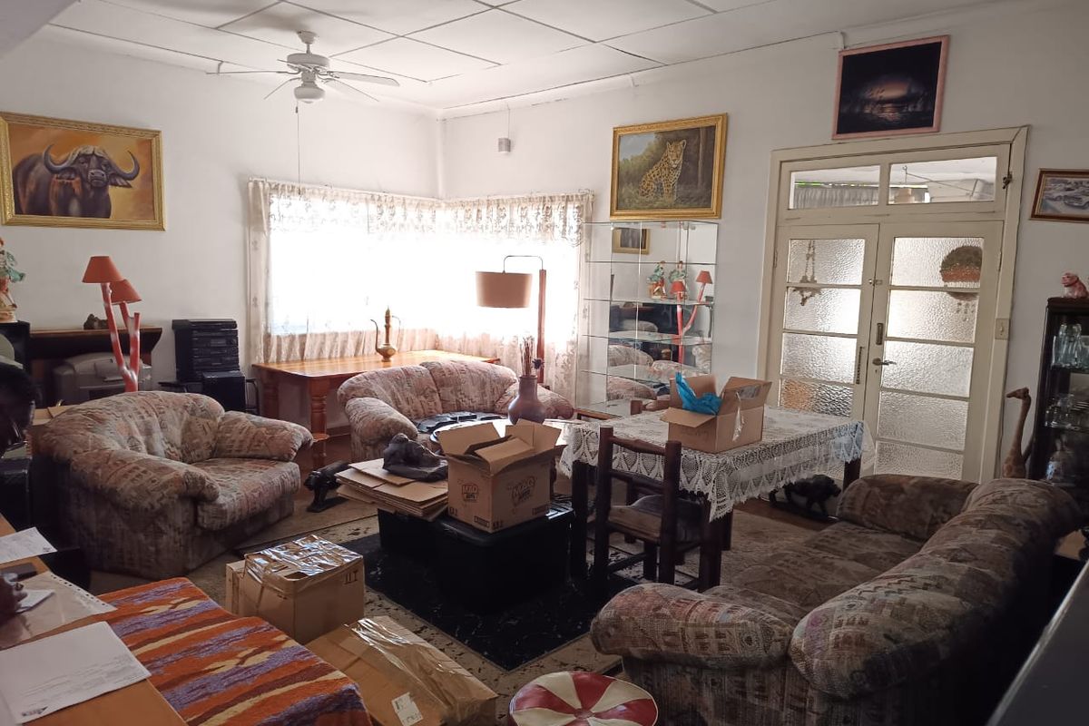 A spacious living room featuring a ceiling fan, tiled ceiling, and glass-panelled double doors, offering a dated interior ready for modernization.