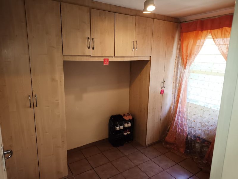 A bedroom featuring extensive light wood built-in cupboards providing ample storage space, tiled flooring, and a window with security bars.