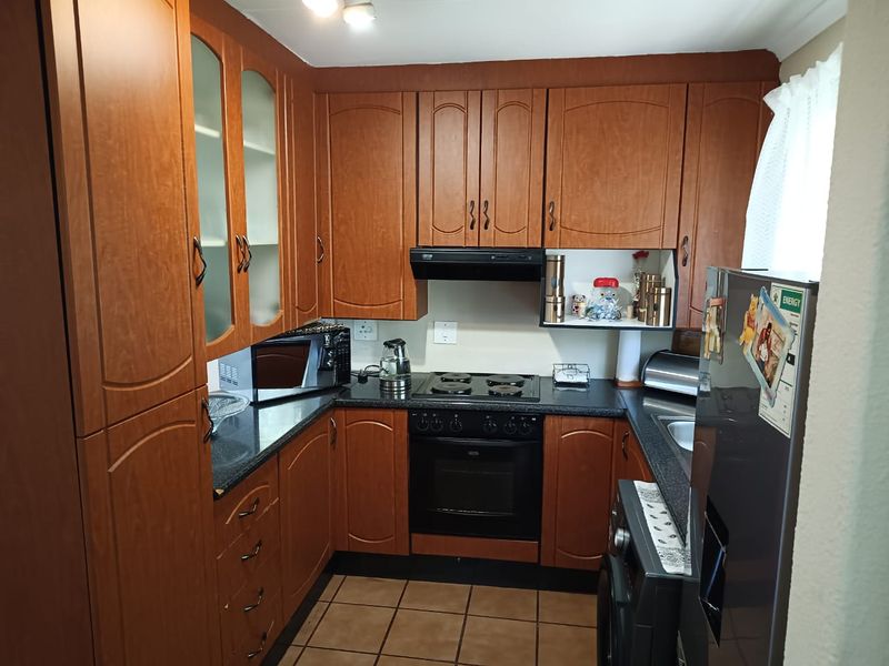 A functional U-shaped kitchen featuring wood-finish cabinetry, dark countertops, built-in oven and hob, and tiled flooring.