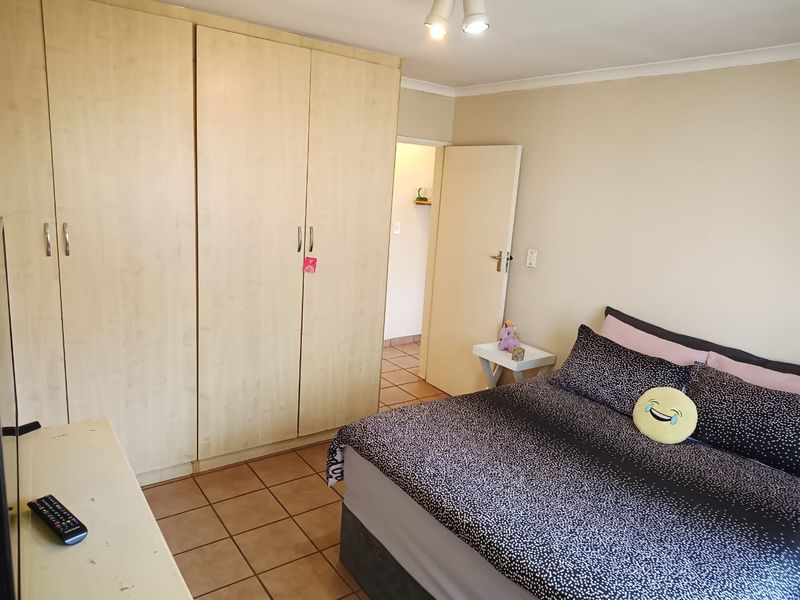 A functional bedroom featuring built-in cupboards, tiled flooring, and neutral wall finishes, providing a practical and comfortable living space.