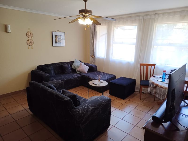 A comfortable living room featuring ceramic tile flooring, a ceiling fan, and large windows that provide ample natural light.
