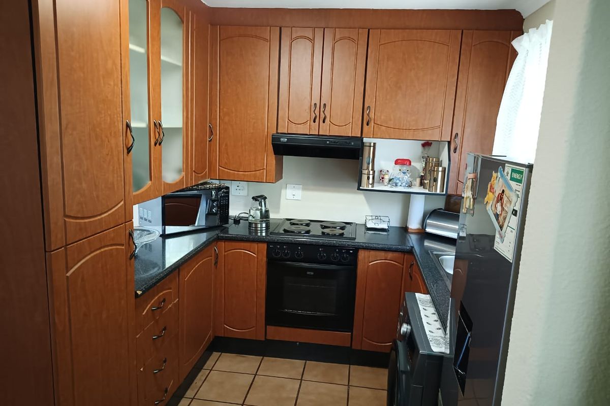 A functional kitchen featuring wood-finish cabinetry, dark laminate countertops, an integrated oven and hob, and tiled flooring.