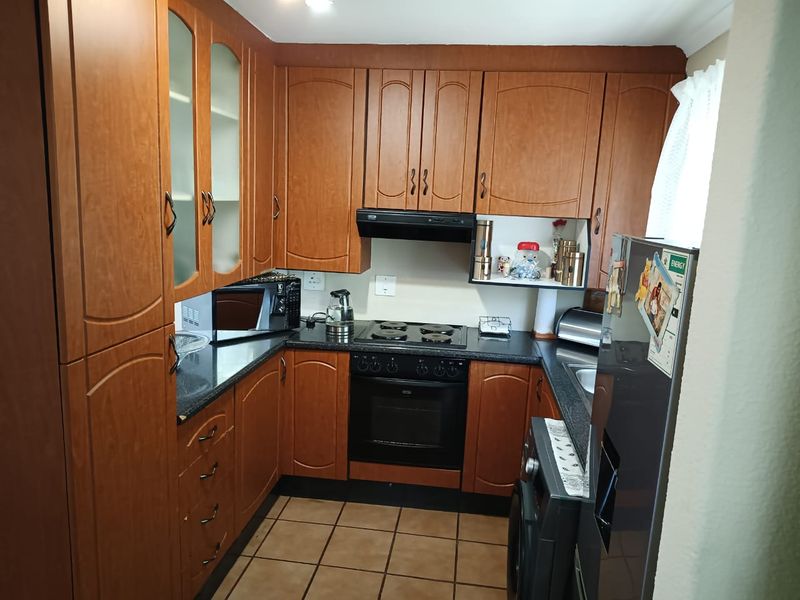 A functional kitchen featuring wood-finish cabinetry, dark laminate countertops, an integrated oven and hob, and tiled flooring.