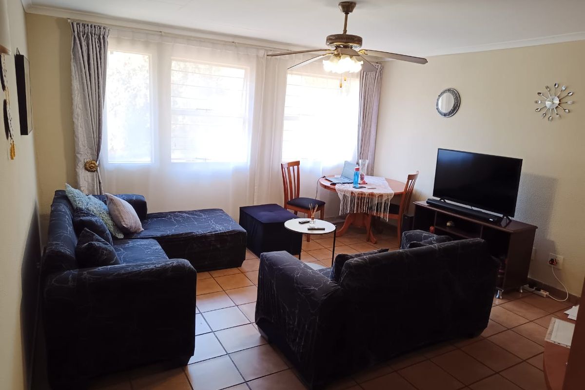 A comfortable living room featuring tiled flooring, a ceiling fan, and large windows that provide ample natural light.