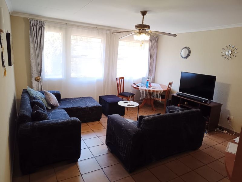 A comfortable living room featuring tiled flooring, a ceiling fan, and large windows that provide ample natural light.