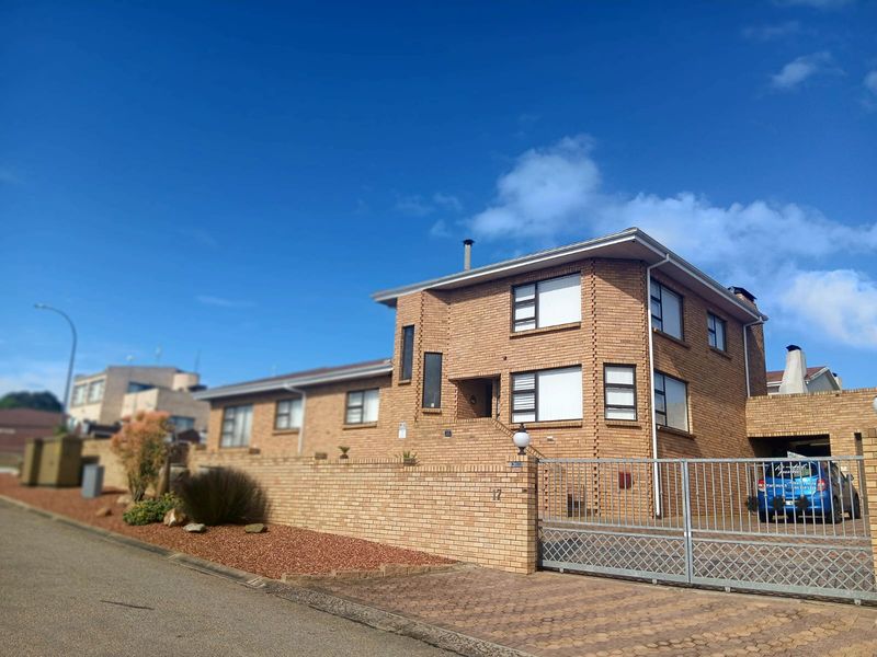A two-story brick residential property featuring a secure metal gate, paved driveway, and established boundary wall, viewed from the street.