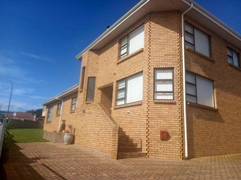 A two-story face brick residential building featuring a paved driveway, external staircase, and aluminium window frames under a clear blue sky.