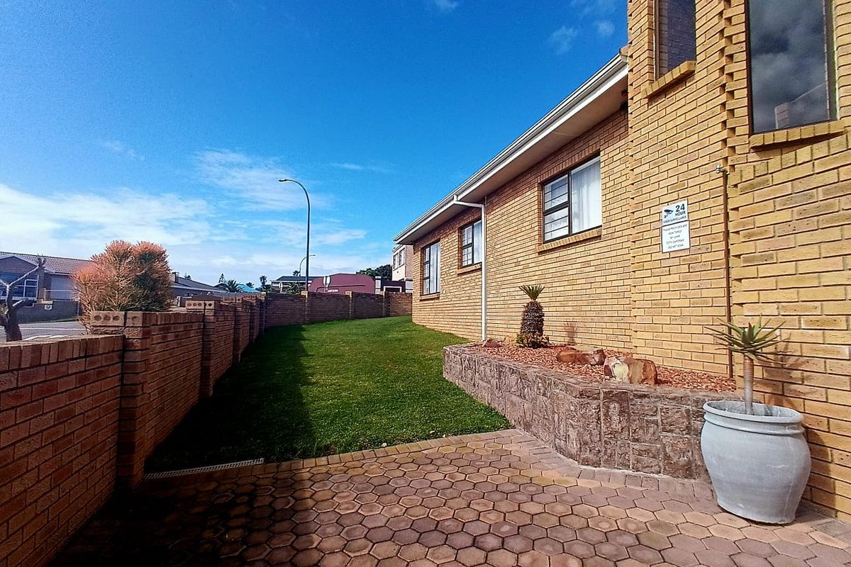 A well-maintained rear exterior featuring a face brick facade, paved patio area, and a neat lawn enclosed by a brick boundary wall.